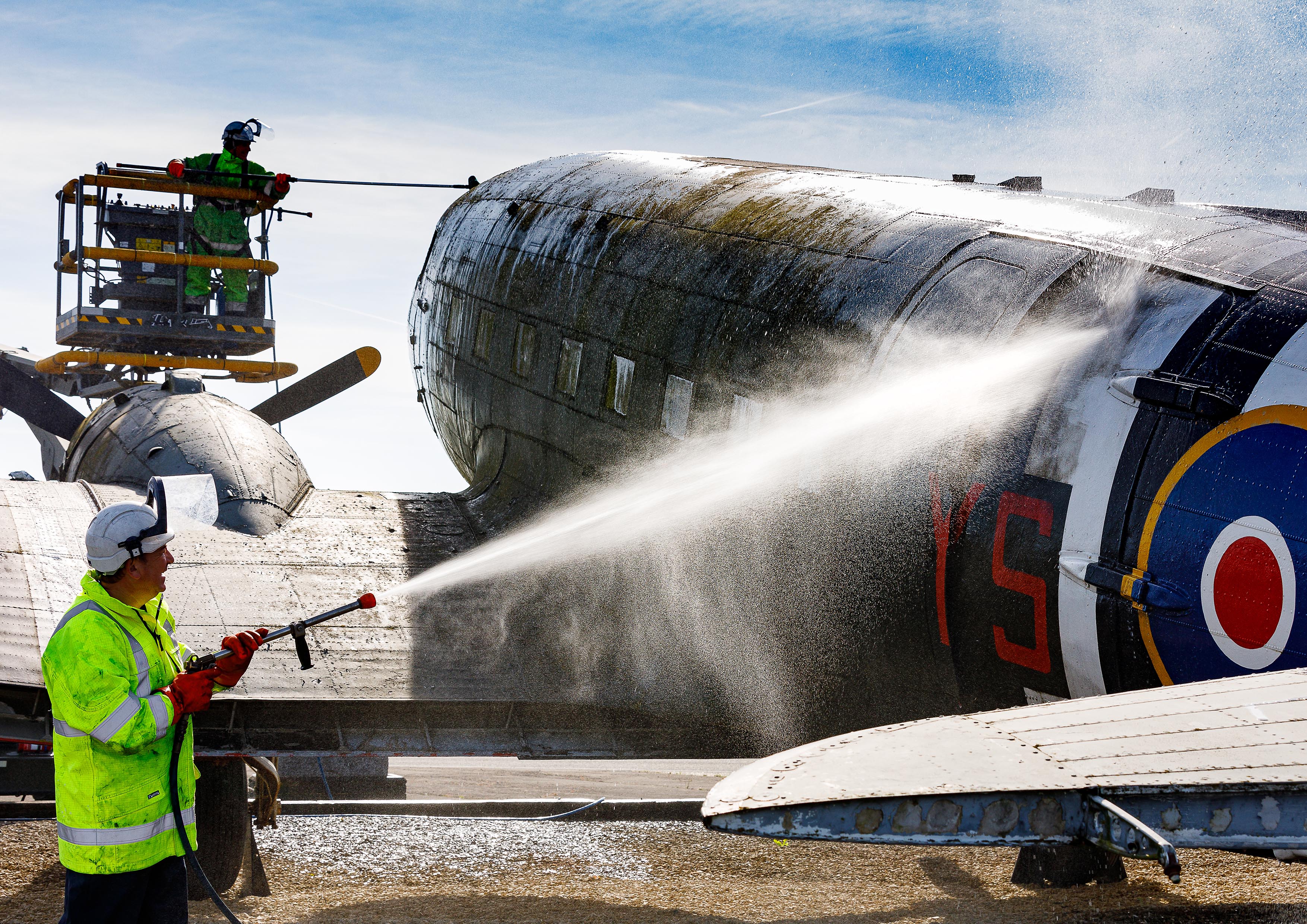 Photo: Members of the Serco Aircraft Wash Team pressure washing the area of the cargo door and brushing organic debris off the area of the flight deck